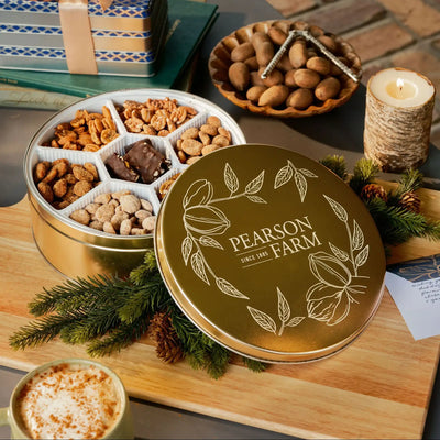 Pearson Farm snack tin with lid on a wooden board, surrounded by a bowl of nuts, a candle, and a gift box.