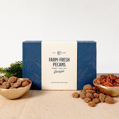 Box of farm-fresh pecans with two bowls of pecans on a beige surface.