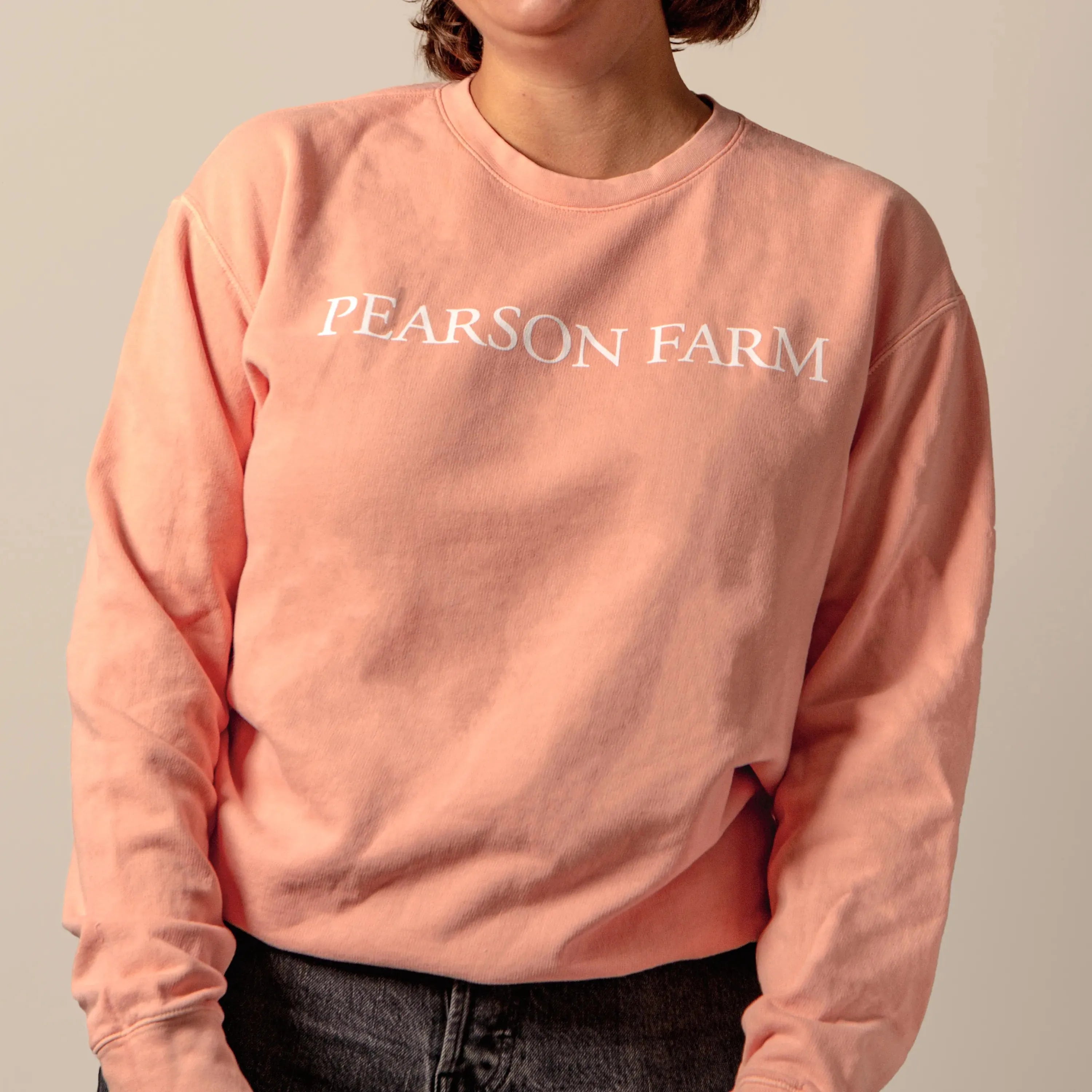Person wearing a peach sweatshirt with 'PEARSON FARM' text on a plain background